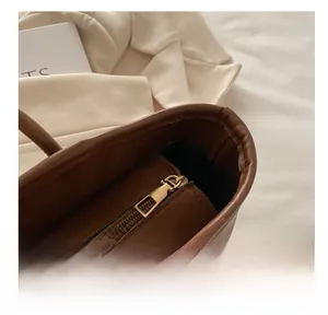 Detail view of the smooth golden metal zipper on a brown leather tote bag with black lining