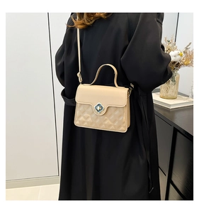 Detail of quilted beige crossbody bag with a black floral clasp and gold-tone hardware