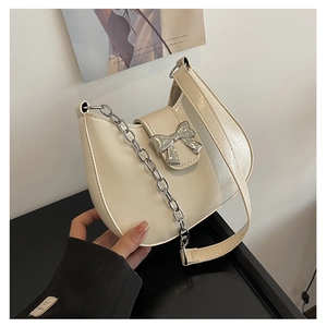 Close-up of cream white half-moon bag with silver metal bow and chain detail