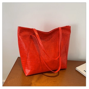 Close-up of red tote bag with crocodile pattern and dual handles for shoulder carry