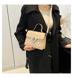 Quilted beige handbag detail with floral metal clasp worn with a black trench coat