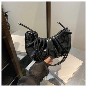 Détail du sac croissant en cuir verni noir avec plis et bandoulière à nœuds