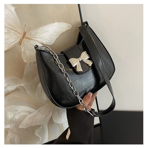 Close-up of black pleated faux leather bag with silver bow buckle and chain strap