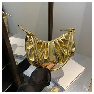 Détail du sac croissant doré plissé avec poignée nouée et finition métallique miroir