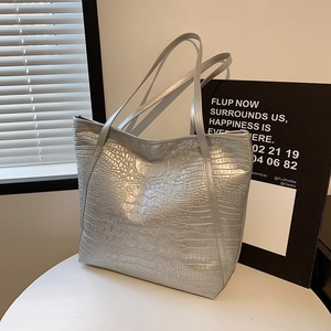 Silver crocodile embossed tote bag with slim handles displayed on a white table