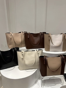 Group display of leather tote bags in various colors on white studio platforms