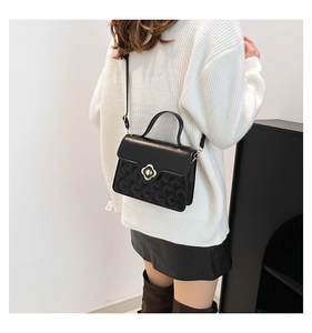Close-up of black quilted crossbody bag featuring a golden floral metal clasp on model