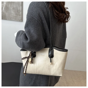 Large capacity tote bag with black piping and tennis racket charm shown on a shoulder