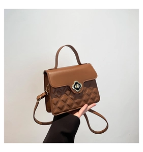 Detail of caramel quilted handbag with clover metal lock and top handle strap
