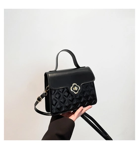 Macro shot of black quilted faux leather handbag with gold clover-shaped metal lock closure