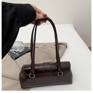 Detail of glossy brown faux leather baguette bag showing vintage texture and strap