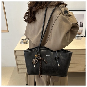 Detail of black tote bag with white FASHION text and elegant braided charm accessory