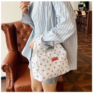Detail of white floral canvas tote bag featuring small pink flowers and red logo tag