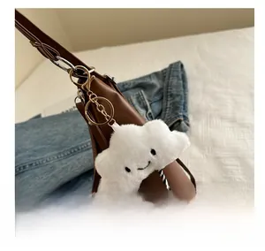 Close-up of white plush cloud charm with smiley face on a brown leather shoulder bag