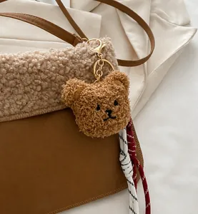Detail of plush brown bear charm with gold metal clasp on a textured fuzzy bucket bag