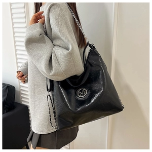 Vue détaillée du sac cabas noir brillant avec bandoulière chaîne et logo M en métal argenté