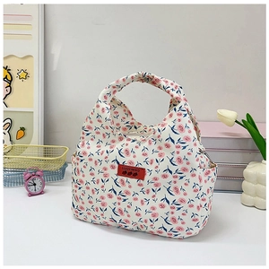 Close-up of floral bento bag with pink rose pattern and red logo tag in a cozy setting
