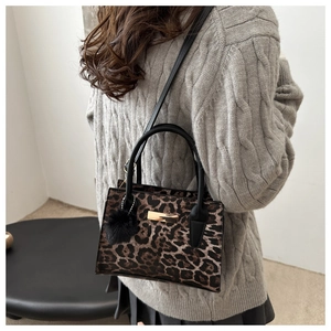 Détail du sac à main léopard avec poignées noires, boucle dorée et pompon en peluche
