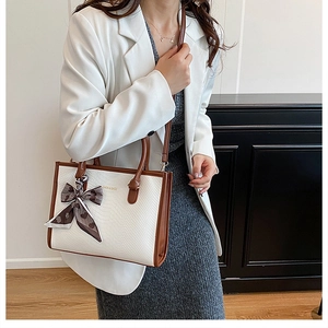 Détail du sac à main avec texture serpent, poignées marron et un foulard en soie
