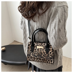 Gros plan du sac à bandoulière léopard porté avec un pull gris et une jupe plissée noire
