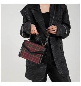 Détail du sac à carreaux vintage rouge et vert porté avec un blazer noir élégant