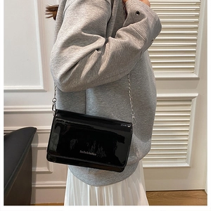 Gedetailleerd beeld van de zwarte laklederen crossbody tas met zilveren ketting op model
