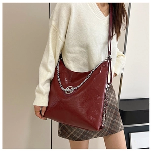 Détail du cabas en cuir verni bordeaux avec chaîne argentée porté par un mannequin