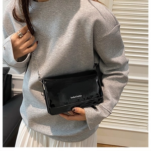Gros plan du sac en cuir verni noir brillant avec inscription Sunila & Fashion et chaîne