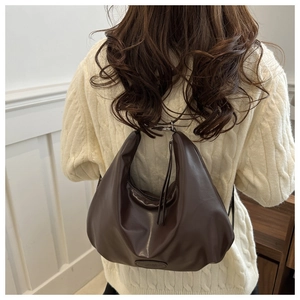 Detail of dark brown leather crescent bag showing smooth texture and strap on a model