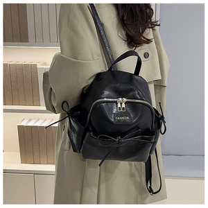 Détail d'un mini sac à dos en similicuir noir avec fermeture dorée et nœud décoratif