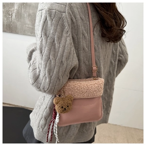 Detail of plush lamb wool bucket bag with cute bear charm and woven tassel strap