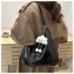 Detail of black leather shoulder bag featuring a white plush cloud charm and embossed logo