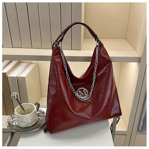 Détail du sac cabas bordeaux brillant avec chaîne argentée et logo M sur étagère