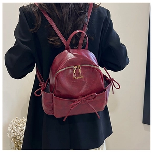 Détail du mini sac à dos bordeaux avec noeud décoratif et fermeture éclair dorée