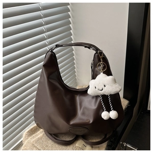 Detail of a dark brown hobo bag with an oval logo and a cute plush cloud charm
