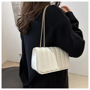 Detail of white pleated shoulder bag with gold chain strap shown on black coat