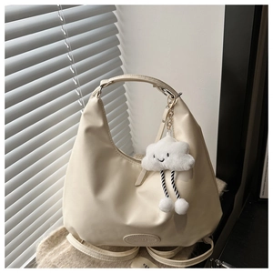Detail of cream leather tote bag with cloud plush pendant on beige knit background