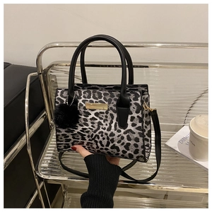 Close-up of leopard print handbag with black pom-pom charm and metallic nameplate detail