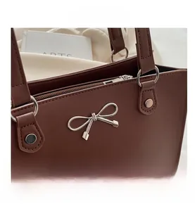 Macro detail of dark brown leather tote with silver metal bow and sturdy stitching finish
