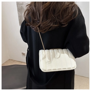 Close-up of a white quilted chain crossbody bag with vertical stitching on a black coat