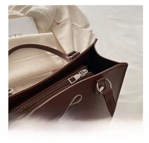 Detail view of smooth metal zipper closure and silver bow on brown leather tote bag