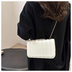 Stylish white quilted chain shoulder bag shown on model with black coat for winter