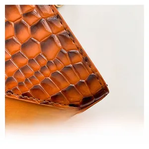 Detailed macro view of orange-brown crocodile pattern faux leather on a luxury handbag