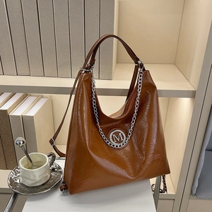 Grand sac cabas en similicuir marron avec chaîne argentée devant une étagère épurée