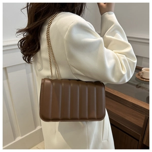 Close-up of brown quilted shoulder bag with gold chain strap on white blazer