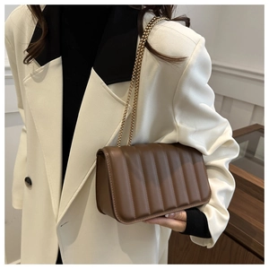 Detail of a brown quilted leather crossbody bag with elegant gold chain strap worn by a model