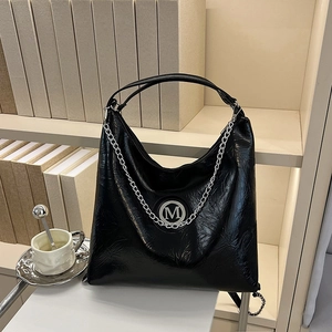 Grand sac cabas noir en cuir avec chaîne argentée et logo M sur bureau élégant