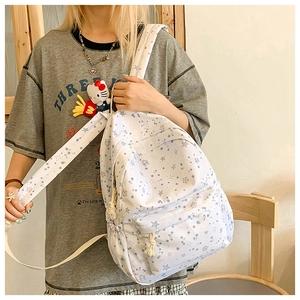 Close-up of white star print canvas backpack with front zipper pocket and plush charms
