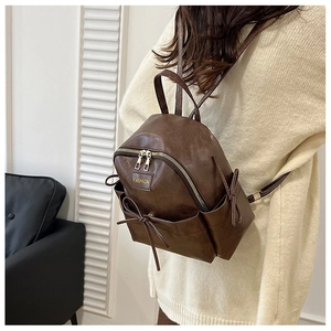Détail du mini sac à dos en cuir PU marron foncé avec nœud décoratif et lettrage en métal