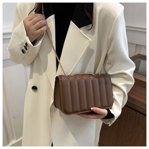 Brown quilted chain bag with vertical pleats styled on a model in white coat